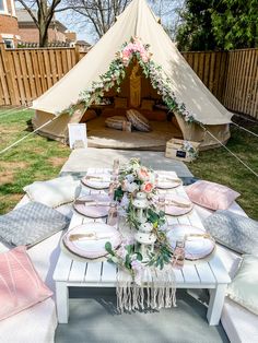 a table set up outside with pink and white flowers on it, in front of a teepee tent