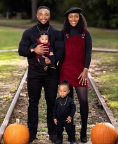 a man, woman and child standing in front of pumpkins on train tracks with their arms around each other