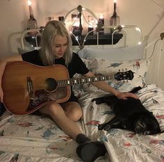 a woman sitting on a bed with a guitar and a dog