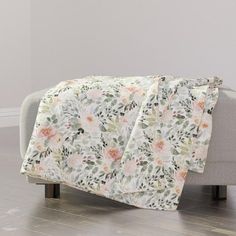 a white couch sitting on top of a hard wood floor next to a flower covered blanket