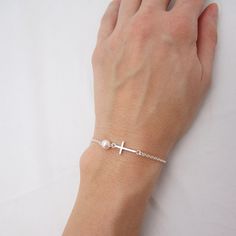 SOLID STERLING SILVER PARTS - A QUALITY BRACELET This lovingly hand-made bracelet is crafted using a solid sterling silver cross that measures just under 3/4 inch long. A 6mm Swarovski pearl comes in your choice of 5 colors. The sturdy sterling silver chain and lobster clasp make this a durable bracelet. Comes in a gift box. SIZING - IMPORTANT: To determine bracelet size, measure snugly around your wrist and add 1/2 inch to get your bracelet size. Do NOT order in your exact wrist measurement. Nickel Free Silver Cross Bracelets, Silver Cross Bracelets For Gifts, Nickel Free Sterling Silver Cross Bracelets, Dainty Sterling Silver Cross Bracelet, Silver Bracelet With Cross Pendant As Gift, Elegant White Cross Bracelet, Hypoallergenic Sterling Silver Pearl Bracelet, Minimalist Sterling Silver Cross Bracelet, Spiritual Sterling Silver Cross Rosary Bracelet