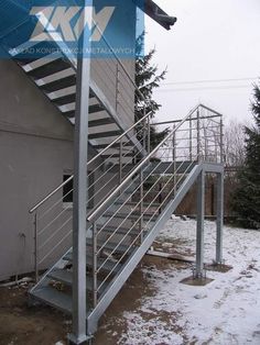 a metal stair rail next to a building with snow on the ground and trees in the background