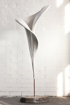 a white sculpture sitting on top of a cement floor next to a brick wall with sunlight streaming through it