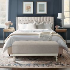 a bedroom with blue walls, white bedding and an upholstered headboard