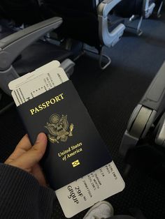 a person holding up a black and white passport in their hand on an airplane seat