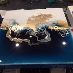 a blue table with gold leaf designs on the top and bottom, sitting on a workbench