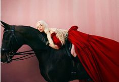 a woman in a red dress riding on the back of a black and white horse