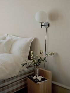 a bed with white sheets and pillows next to a night stand with flowers on it