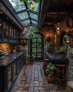 an outdoor kitchen with stone walls and flooring is lit by hanging lights from the ceiling