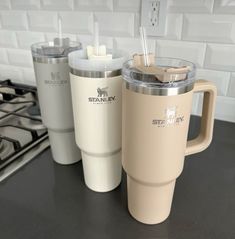 three coffee mugs sitting on top of a counter next to each other in front of a stove