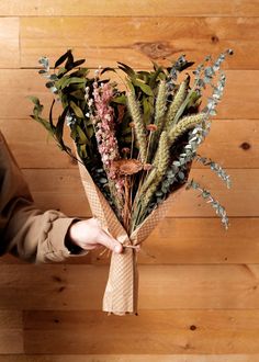 a person holding a bunch of flowers on top of a wooden floor next to a wall