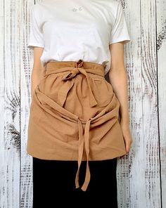 a woman standing in front of a white wooden wall wearing an apron with a tie