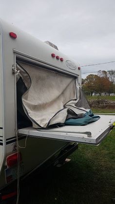 an rv is parked on the grass with it's door open and tarp over