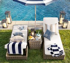 two wicker lounge chairs with pillows and an umbrella on the grass near a pool