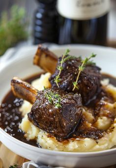 a white plate topped with meat and mashed potatoes next to a bottle of wine