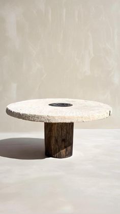 a white table with a wooden base and a black hole in the center, on a plain surface