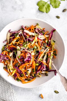 a white bowl filled with coleslaw, carrots and sprouts on top of a table