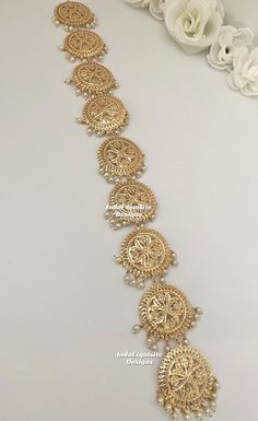 a gold bracelet with intricate designs and pearls on the sides, along with flowers in the background