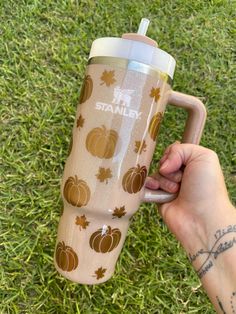 a person holding a coffee cup in their hand on the grass with pumpkins and leaves all over it