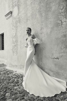 a woman in a white dress leaning against a wall