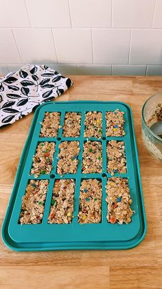 a blue tray filled with granola bars on top of a wooden table next to a bowl of cereal