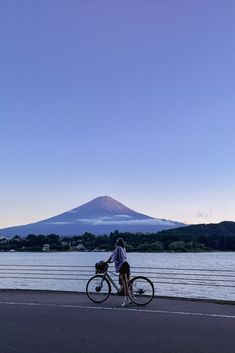 a person riding a bike next to a body of water with a mountain in the background