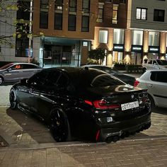 a black car parked on the side of a street next to tall buildings at night