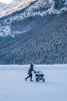 a woman pushing a stroller in the snow with mountains in the backgroud