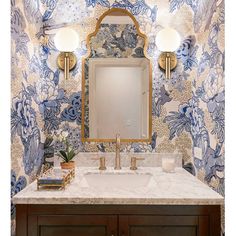 a bathroom with blue and white wallpaper, gold fixtures and a large mirror above the sink