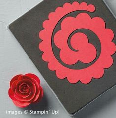 a red rose sitting next to a black box with a paper cut out of it