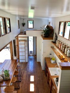 the interior of a tiny house with wood floors and windows on each side, looking down into the kitchen