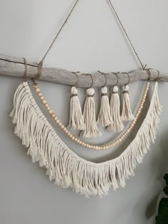 a white wall hanging with tassels and beads on the end, along with a plant