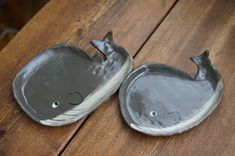 two gray whale shaped dishes sitting on top of a wooden table