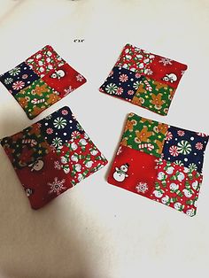 four red and green square coasters with snowflakes on the top, one is blue