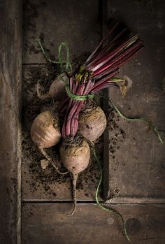 there are some onions on the floor with dirt around them and one is purple in color