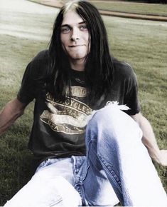 a man with long hair sitting in the grass