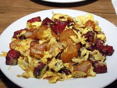 a white plate topped with eggs, potatoes and bacon on top of a wooden table