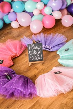 there are many different colored tutu skirts on the floor next to balloons and a sign