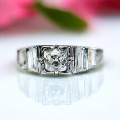 a diamond ring sitting on top of a table next to a pink flower with petals in the background