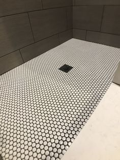 a tiled shower stall with white and gray tiles on the floor, and a black square drain in the middle