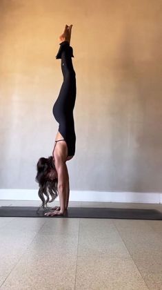 a woman doing a handstand on the floor in front of a wall with her legs up