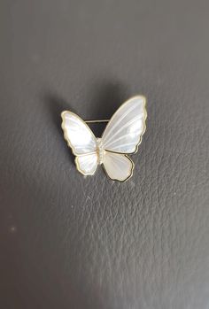 Delicately crafted, this Mother of Pearl Butterfly Brooch is designed with an asymmetrical style, adding a touch of elegance and charm to any outfit. Its petite size makes it suitable for daily wear, adding a subtle yet refined sparkle to your attire. Made with genuine mother of pearl, cubic zirconia, and copper plated in gold, this brooch is a beautiful blend of nature-inspired beauty and luxurious detail. Size: 1.1 in * 1.1 in (Handmade, the actual size can vary) Material: Mother of Pearl, Cub Elegant White Enamel Pin For Gift, Wedding Enamel Pin Brooch, Formal White Enamel Pin Brooch, Formal White Enamel Pin, Elegant Butterfly Shaped Pins, White Brooch Jewelry Gift, White Butterfly Brooches For Gifts, Elegant Silver Enamel Pin For Weddings, White Anniversary Brooch Jewelry