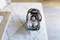 a baby sitting in a car seat on top of a white rug next to a wooden table