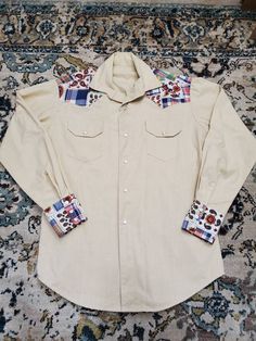 "Amazing one of a kind vintage handmade western top! Probably from the 70's! Thick textured cream fabric with printed patchwork accents (floral, paisley, plaid) on sleeve cuffs and around collar. Cute horseshoe snaps! Down front and 3 on each sleeve cuff. Pockets in front. In Excellent Vintage Condition with no visible flaws! Measurements: Chest: 44\" Length: 29\" Shoulders: 18.5\" Sleeve Length: 33.5\"" Western Style Cotton Shirt For Spring, Vintage Cotton Tops For Rodeo, Cotton Button-up Country Tops, Country Style Button-up Cotton Tops, Country Style Cotton Button-up Tops, Fitted Cotton Western Top, Fitted Cream Tops With Button Cuffs, Fitted Patchwork Button-up Shirt, Retro Long Sleeve Patchwork Shirt