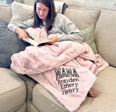 a woman sitting on a couch reading a book under a pink sherpam blanket