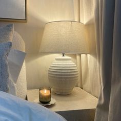 a white lamp sitting on top of a table next to a bed with pillows and blankets