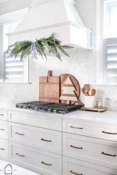 a kitchen with white cabinets and wooden cutting boards on the stove top, surrounded by greenery