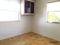 an empty room with wooden floors and two windows in the corner that have no curtains on them