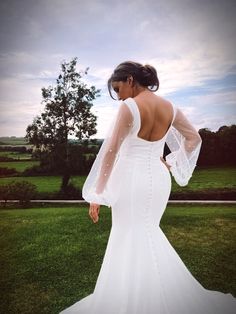 a woman in a white wedding dress standing on the grass with her back to the camera