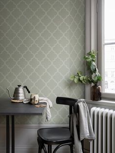 a table and chair in front of a wall with a green trellis pattern on it